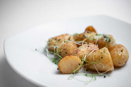 closeup of tasty roasted potatoes with microgreen on plate on white backgroundの写真素材