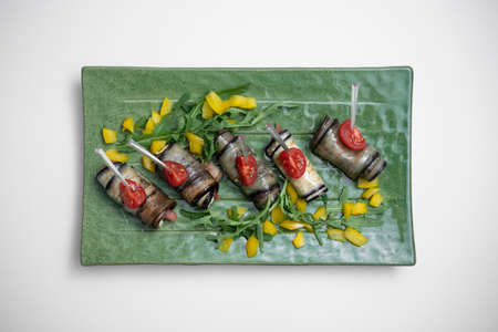 top view of eggplant rolls with cream cheese on green plate on white backgroundの写真素材