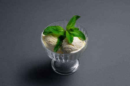 tasty vanilla ice cream with fresh mint in glass bowl on black backgroundの写真素材
