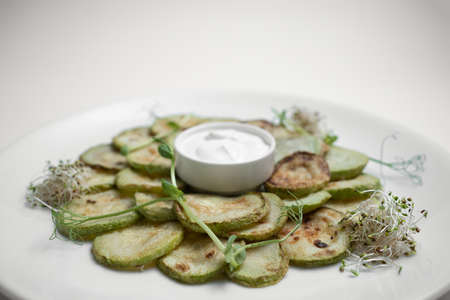 closeup of fried zucchini slices with sour cream on plate on white backgroundの写真素材