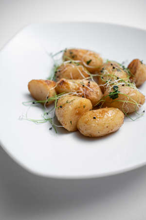 closeup of tasty roasted potatoes with microgreen on plate on white backgroundの写真素材