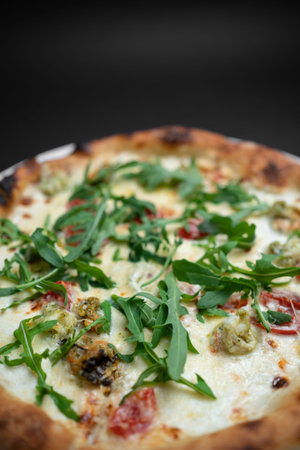 closeup of seafood pizza with shrimp, mussels and arugula on black background