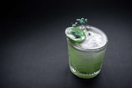 fresh green kiwi kick alcohol cocktail drink in wineglass on black backgroundの写真素材