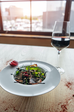fresh salad with arugula, meat ham and strawberry and glass of red wine on tableの写真素材
