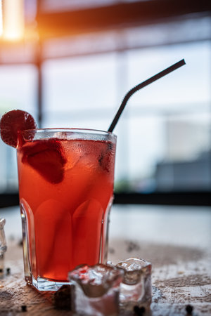 closeup of red lemonade drink with strawberry in glass and ice on wooden tableの写真素材