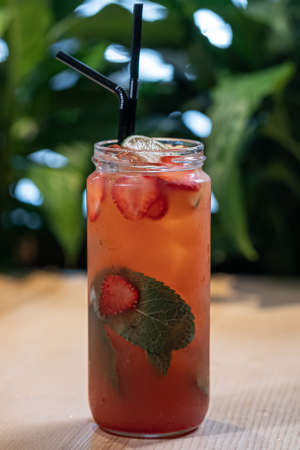 strawberry lemonade drink with mint in glass bottle and ice near green plantの写真素材