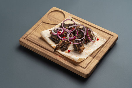 shashlik or grilled meat with onion on pita on wooden board on grey backgroundの写真素材
