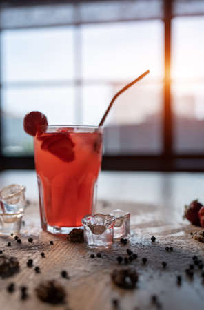 closeup of red lemonade drink with strawberry in glass and ice on wooden tableの写真素材