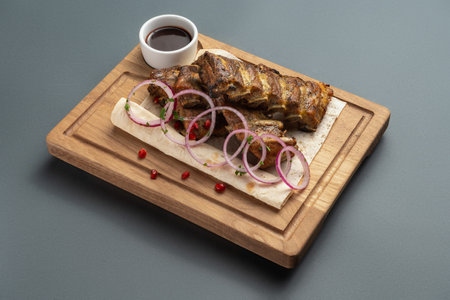 shashlik or grilled meat ribs with sauce and onion on pita on wooden boardの写真素材