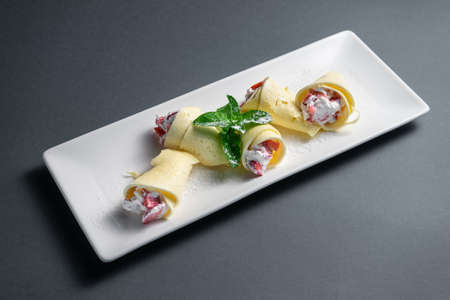 thin pancake rolls with cottage cream cheese and strawberry on black backgroundの写真素材