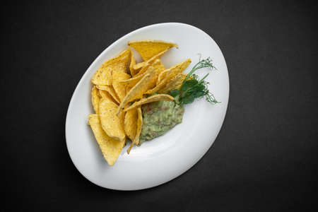 top view of guacamole dip in bowl with avocado and nachos on black backgroundの写真素材