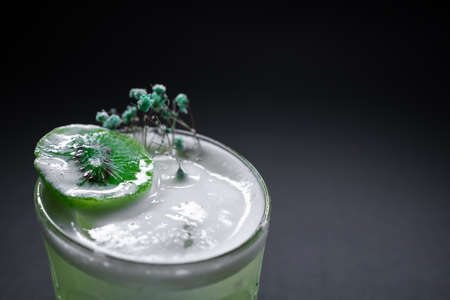 fresh green kiwi kick alcohol cocktail drink in wineglass on black backgroundの写真素材