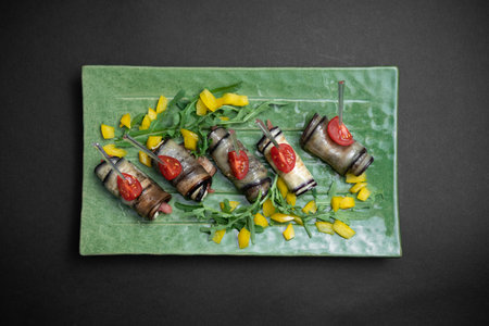 top view of eggplant rolls with cream cheese on green plate on black backgroundの写真素材