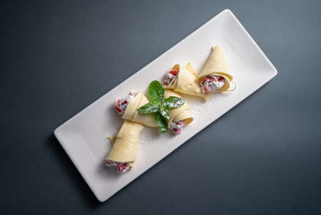 top view of thin pancake rolls with cottage cheese and strawberry on white plateの写真素材
