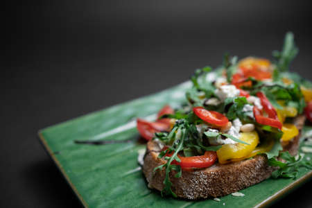 bruschetta or toast bread with arugula, tomatoes and cheese on black backgroundの写真素材