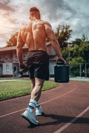 muscular athlete holding protein whey drink in black container or shaker outdoorの写真素材