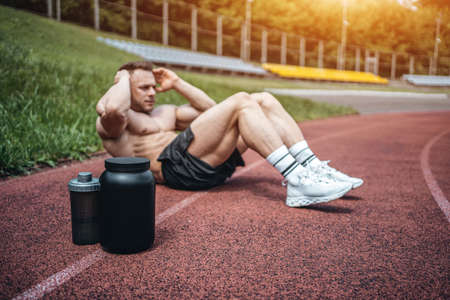protein whey drink in black container and muscular athlete exercising outdoorの写真素材
