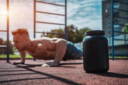 protein whey drink in black container and muscular athlete exercising outdoorの写真素材