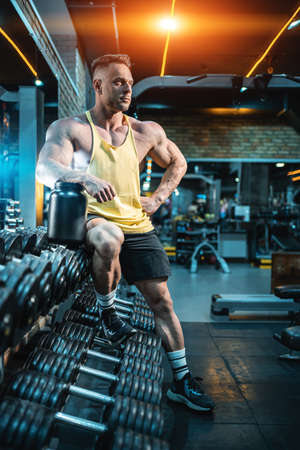 muscular bodybuilder male with protein whey powder in black container in gymの写真素材