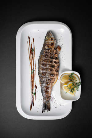 close up of whole grilled stuffed fish sea bass with lemon on black backgroundの写真素材