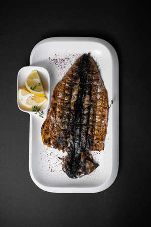top view of grilled mackerel fish with lemon on white plate on black backgroundの写真素材