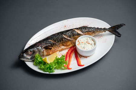 closeup of baked mackerel fish with sauce on white plate on black backgroundの写真素材