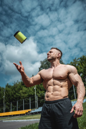 muscular bodybuilder male throw up container with protein whey powder outdoorの写真素材