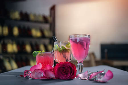 pink lemonade drink in glass and alcoholic cocktail with rose petals on tableの写真素材