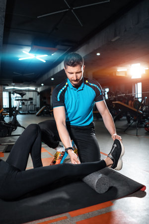 young female relaxing with myofascial release roller with trainer in gym