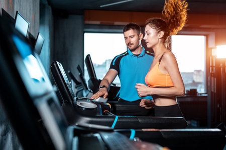 young beautiful woman has workout on treadmill with personal trainer and running