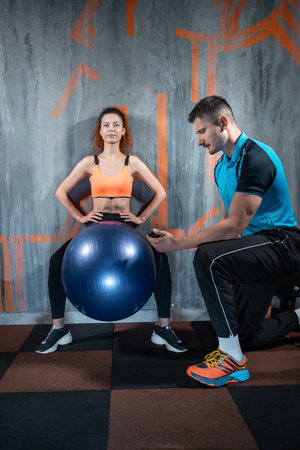young female has workout and exercising with fit ball and personal trainer gym