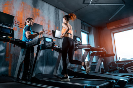 young beautiful woman has workout on treadmill with personal trainer and running