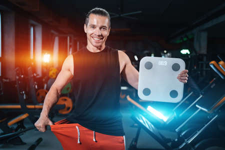 young attractive athlete male weight with scale in gym and dietingの写真素材