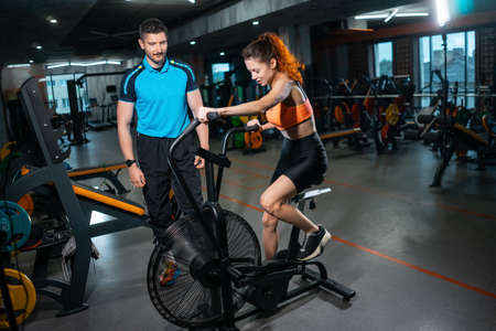 female has workout and training on exercise bike with personal trainer in gymの写真素材