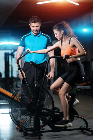 female has workout and training on exercise bike with personal trainer in gymの写真素材
