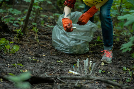 volunteer cleaning up used syringe in park and standing by bunch of garbage bagの写真素材