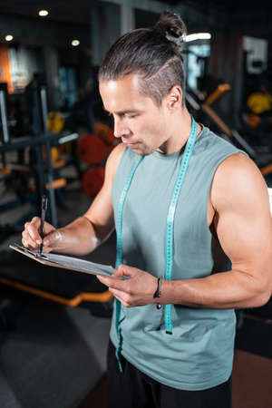 young attractive man personal trainer planning workout with clipboard in gymの写真素材