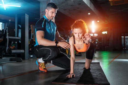young woman exercising quadruplex with personal trainer in gymの写真素材