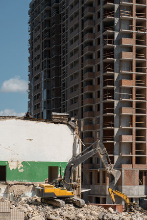 demolition old building by excavator near new construction of modern skyscraperの写真素材