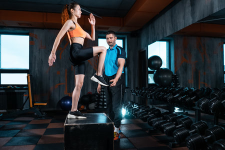 athlete female has exercising lunges on step box with personal trainer in gymの写真素材