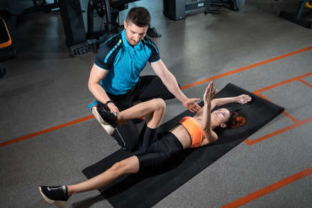young woman exercising dead bug with personal trainer in gymの写真素材