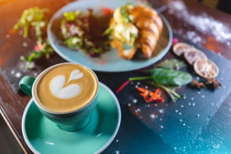 croissant sandwich breakfast with green salad and poached eggs, bacon and coffeeの写真素材