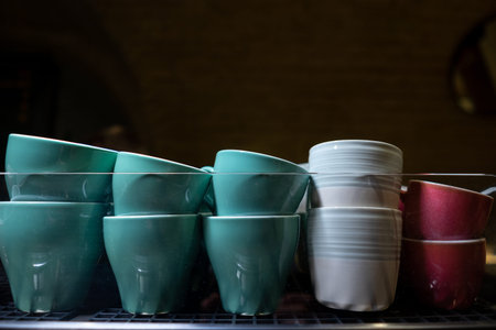 set of ceramic colored cups or mugs heating on professional coffee machine