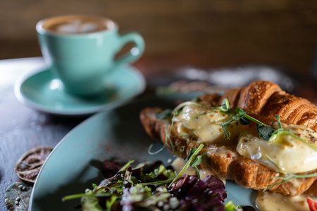croissant sandwich breakfast with green salad and poached eggs, bacon and coffeeの写真素材