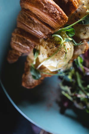 fresh croissant sandwich breakfast with green salad and poached eggs, baconの写真素材