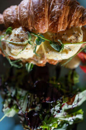 fresh croissant sandwich breakfast with green salad and poached eggs and baconの写真素材