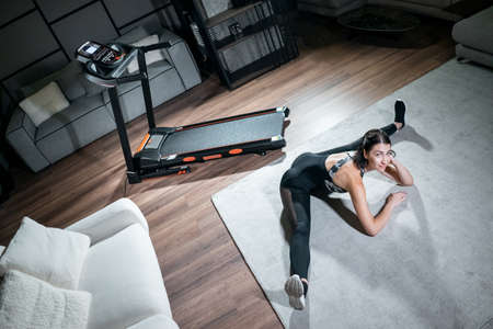 cheerful female stretching and preparing for cardio workout on treadmill at homeの写真素材