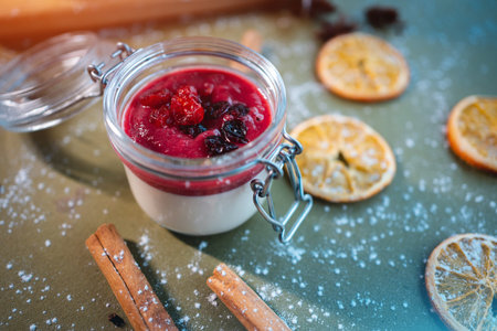 closeup of berry panna cotta dessert with cherry sauce in glass jar on table