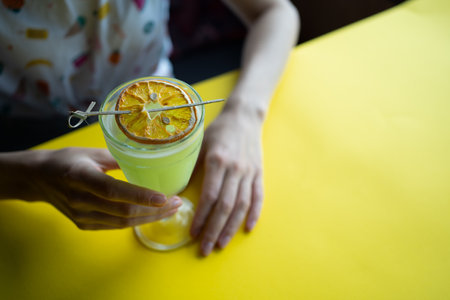 female drinking fresh green cocktail with pisang liquor, orange in bar or cafeの写真素材