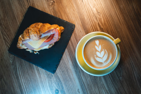 fresh cappuccino or latte coffee with croissant sandwich on wooden table in cafeの写真素材